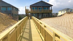 Un muelle de madera que lleva a una casa de playa de dos pisos con balcón.