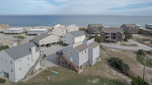 A coastal residential area with multiple two-story houses, some with balconies, and a beach in the background. - 5793- Beachy Keen - South Nags Head Retreat Steps From Beach (Nags Head)