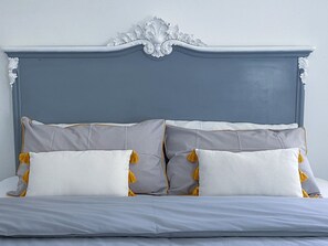 Un letto con una testiera grigia e cuscini bianchi con pon pon gialli.