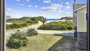 Eine Küstenansicht mit einem Sandweg, der zu Dünen, einem Strand und einem Gebäude mit geneigtem Dach führt.