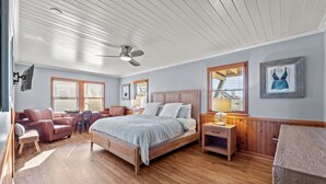 Une chambre à coucher avec un lit en bois, un bureau, une chaise, une table de chevet et un ventilateur de plafond.