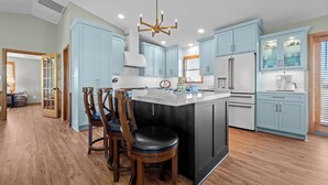 Une cuisine moderne avec des meubles de couleur bleu clair, un îlot central doté de tabourets de bar et un lustre.