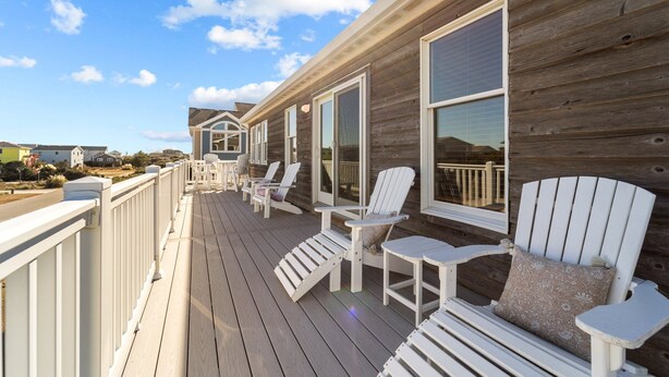 Une terrasse en bois avec des chaises Adirondack blanches et une rambarde.
