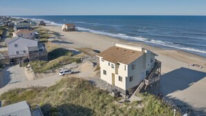 A coastal property with a beach view, a small building with a staircase, and a sandy area with a few vehicles. - 6300- Sea Master, OBX Oceanfront Escape | Jacuzzi & Views (Nags Head)