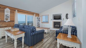 A living room with striped sofas, a fireplace, a television, and a bookshelf. - 6300- Sea Master, OBX Oceanfront Escape | Jacuzzi & Views (Nags Head)