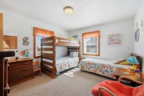 Une chambre avec des lits superposés, un bureau, une chaise et une petite table avec une lampe.