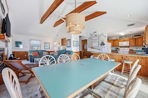 Un salon spacieux avec une grande table, des sièges confortables, un ventilateur de plafond et un coin cuisine doté de meubles en bois.