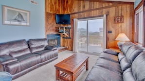 A living room with a fireplace, leather sofas, a wooden coffee table, and a television. - 6504- Eagle's Nest - Quiet Ocean View Escape | Walk to Beach (Nags Head)