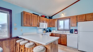 A kitchen with wooden cabinets, a white refrigerator, and a bar stool area. - 6504- Eagle's Nest - Quiet Ocean View Escape | Walk to Beach (Nags Head)