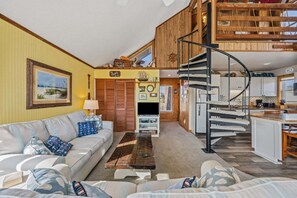 A spacious living area with a sofa, coffee table, and a spiral staircase leading to an upper level. - 7026- Southwind, | Oceanside | Rodanthe | Sleeps 4 (Rodanthe)