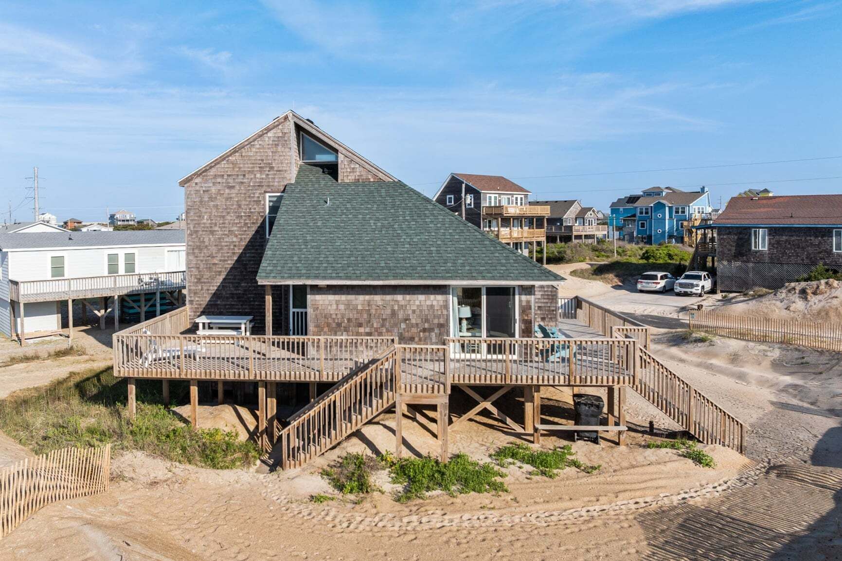 A beachfront house with a wooden deck, a small balcony, and a large window.