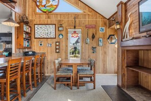 A wooden interior with a dining area, bookshelves, a clock, and a sign reading 'RODANTHE.' - 7026- Southwind, | Oceanside | Rodanthe | Sleeps 4 (Rodanthe)