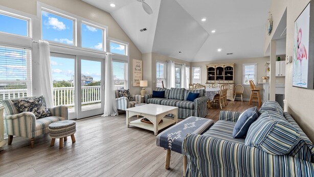 Ein geräumiges Wohnzimmer mit hoher Decke, großen Fenstern und Blick ins Freie.