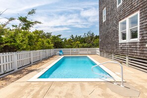 A rectangular swimming pool with a white deck and metal handrails, surrounded by a white picket fence and trees. - 7219- C-Waves, Salvo Beach House | Pool, Hot Tub & Walk to Beach (Salvo)