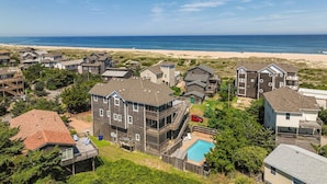 Un quartier résidentiel situé sur la côte, avec plusieurs maisons, une piscine et une plage en arrière-plan.
