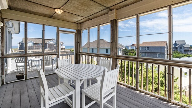 Une terrasse extérieure couverte, dotée d’une table et de chaises, de grandes fenêtres et offrant une vue sur les maisons voisines.