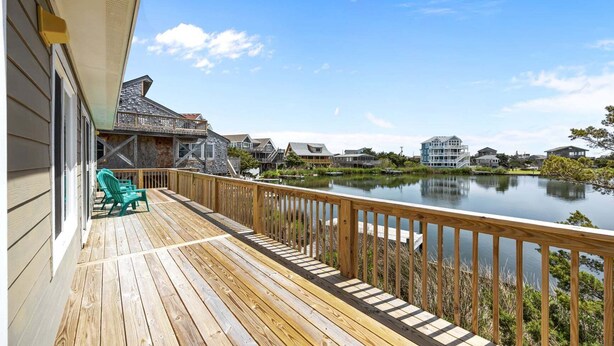 Une terrasse en bois avec des chaises, une vue sur un lac paisible et des maisons en arrière-plan.