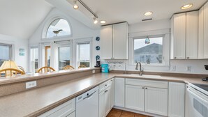 Eine moderne Küche mit weißen Schränken, einem Geschirrspüler und einem großen Fenster mit Ausblick.