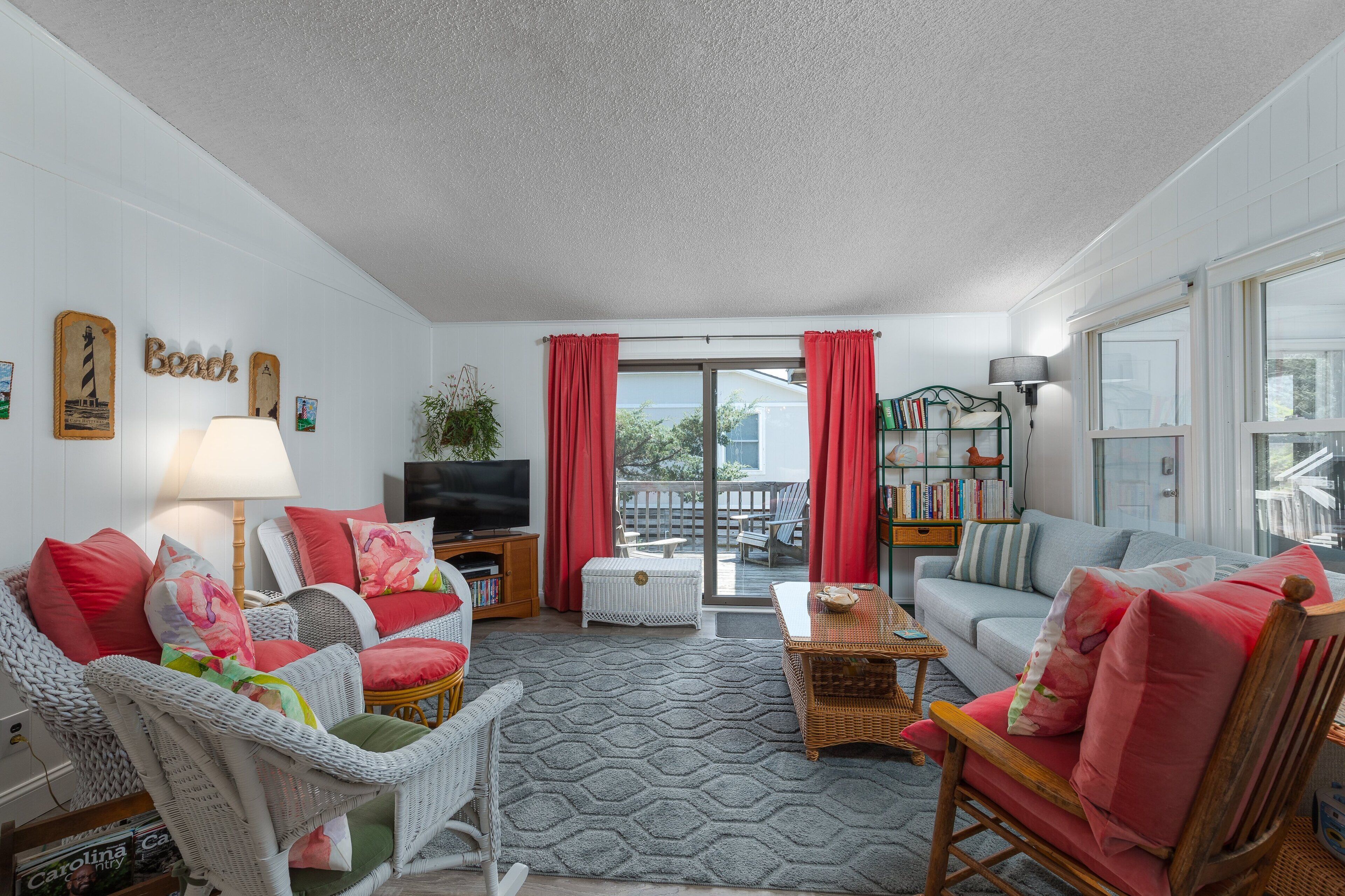 Ein Wohnzimmer mit Rattanmöbeln, einem Fernseher und einem Balkon mit roten Vorhängen.