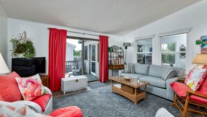 A living room with a sofa, a coffee table, a TV, and a bookshelf. - 7563- Sea Dreams, 200 Yards to Beach | Pool Access in Avon (Avon)