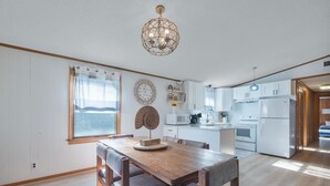 Une cuisine moderne avec des meubles blancs, une table à manger en bois et un luminaire suspendu.