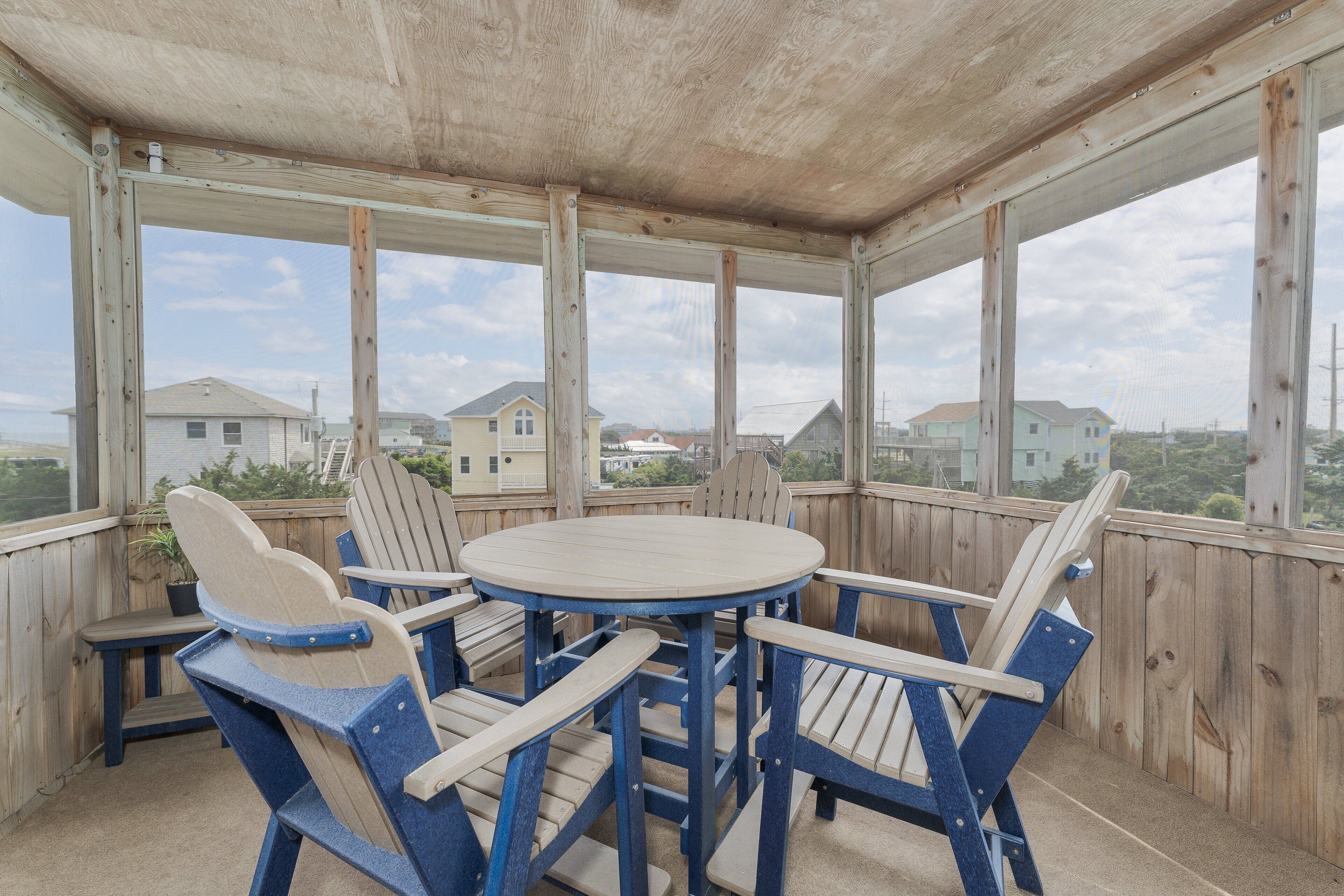 A covered outdoor seating area with wooden chairs and a table, overlooking a residential neighborhood.
