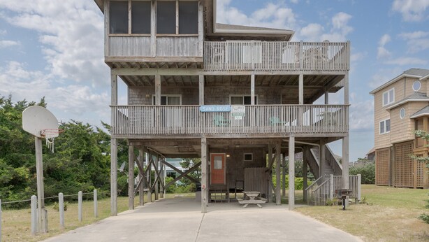 Un edificio de madera de varios pisos, con un balcón, un aro de baloncesto y una mesa de picnic.