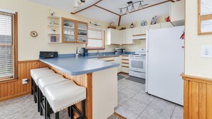Cocina compacta con una isla central, taburetes de madera, horno empotrado y refrigerador blanco.