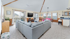 Una sala de estar amplia con un sofá seccional gris grande, un televisor de pantalla plana y una zona de comedor con una mesa y sillas de madera.