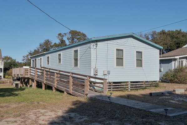 A light blue single-story house with a wooden deck and a ramp leading to the front door.