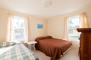 A room with two beds, a small table, and a window with curtains.