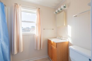 A bathroom with a window, a sink, a mirror, and a toilet.
