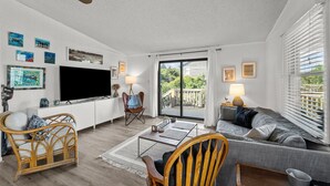 A modern living room with a flat-screen TV, wicker chairs, a grey sofa, and a balcony with a view. - 7850- Nepenthe - Charming Frisco Getaway Near The Beach (Frisco)