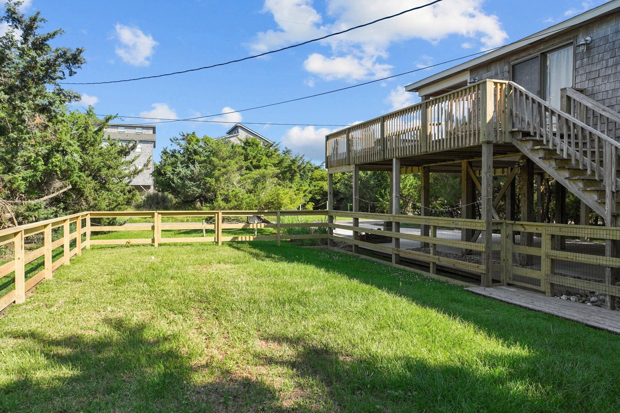 A wooden deck with a staircase leading to a balcony, surrounded by a fenced yard and trees.