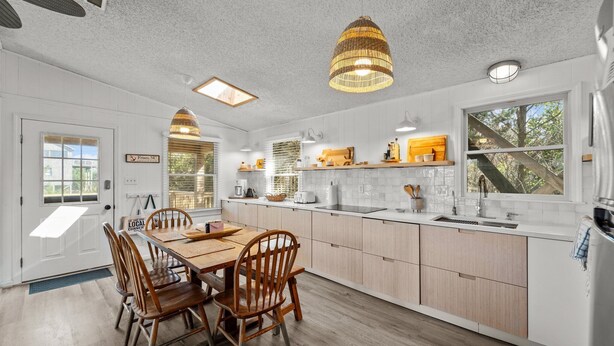 A modern kitchen with white cabinetry, a wooden dining table, and pendant lighting. - 7850- Nepenthe - Charming Frisco Getaway Near The Beach (Frisco)
