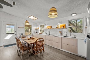 A modern kitchen with white cabinetry, a wooden dining table, and pendant lighting. - 7850- Nepenthe - Charming Frisco Getaway Near The Beach (Frisco)