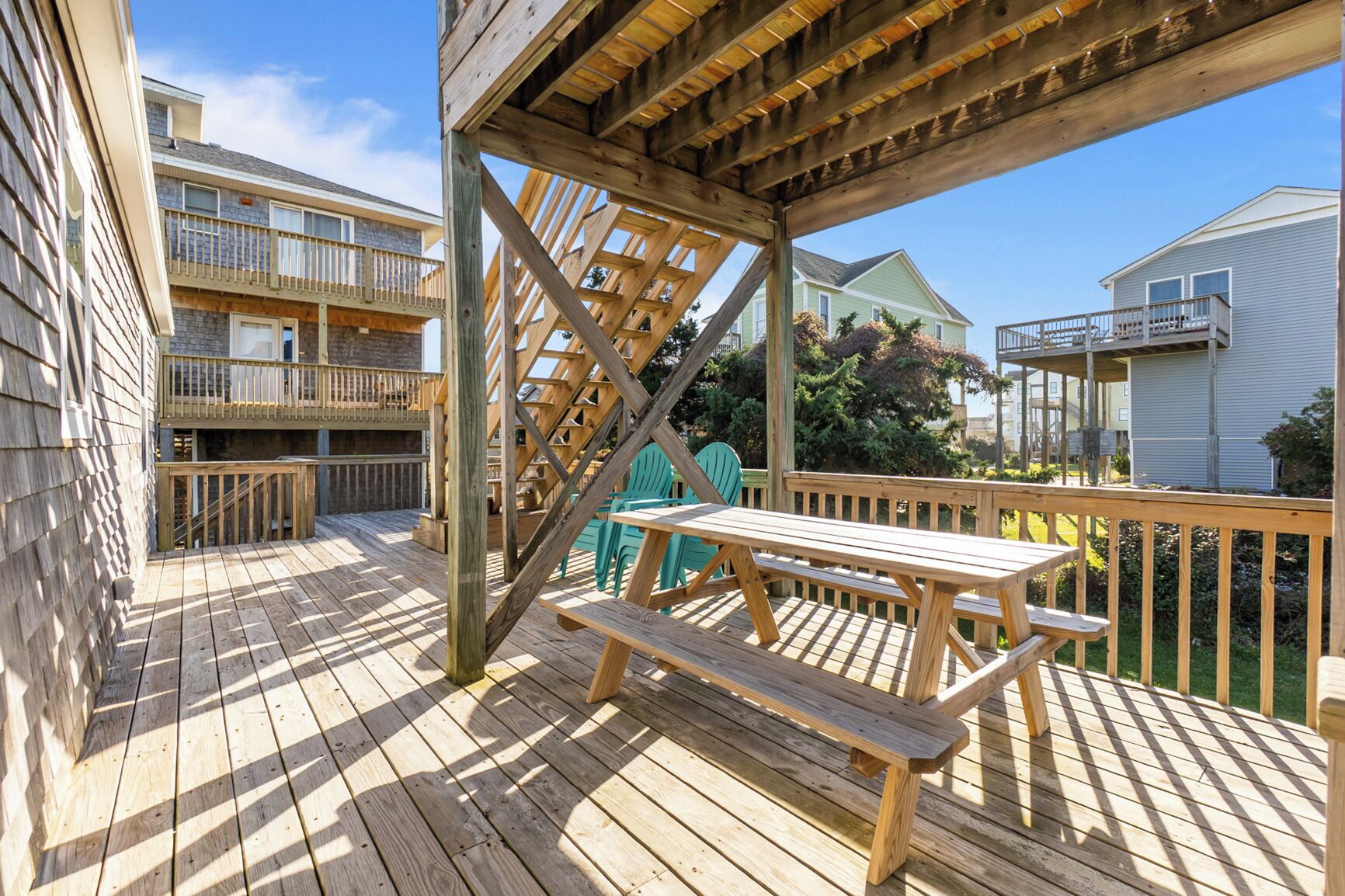 A wooden deck with a picnic table and chairs, surrounded by a wooden railing and a staircase.