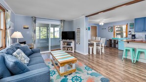 Ein Wohnzimmer mit Sofa, Couchtisch und Fernseher. Es gibt einen Essbereich mit Tisch und Stühlen. Die Küche verfügt über eine Arbeitsfläche und Hocker.