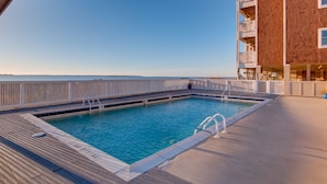 Area piscina con vista aperta sull'oceano, un solarium in legno e un edificio in mattoni con balconi.