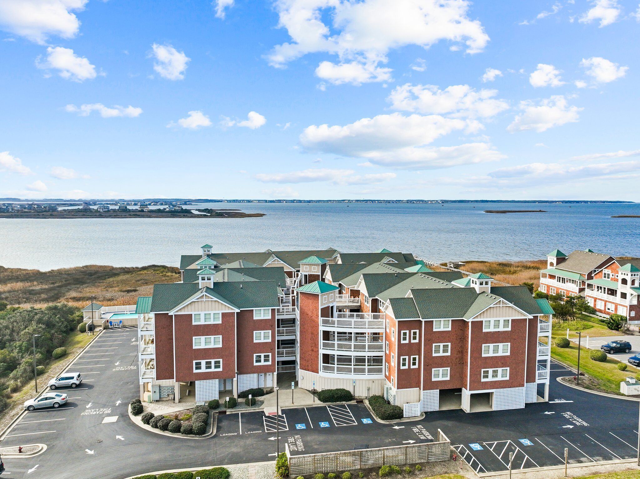 A coastal hotel with multiple buildings, a parking lot, and a view of the sea.