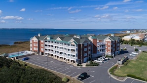 A multi-story hotel with a pool, parking lot, and a view of the ocean. - C309-Sounds Good 309 - Soundfront Nags Head Condo With Sunsets (Nags Head)