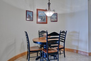 A dining area with a round table, four chairs, and a hanging light fixture. There are three framed pictures on the wall. - C309-Sounds Good 309 - Soundfront Nags Head Condo With Sunsets (Nags Head)