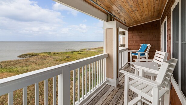 A wooden deck with a white railing, a table, and two chairs overlooking a beach. - C309-Sounds Good 309 - Soundfront Nags Head Condo With Sunsets (Nags Head)