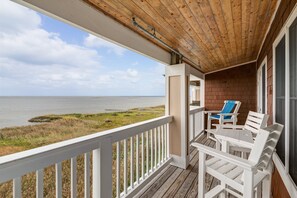 Une terrasse en bois avec une balustrade blanche, une table et deux chaises, donnant sur une plage.