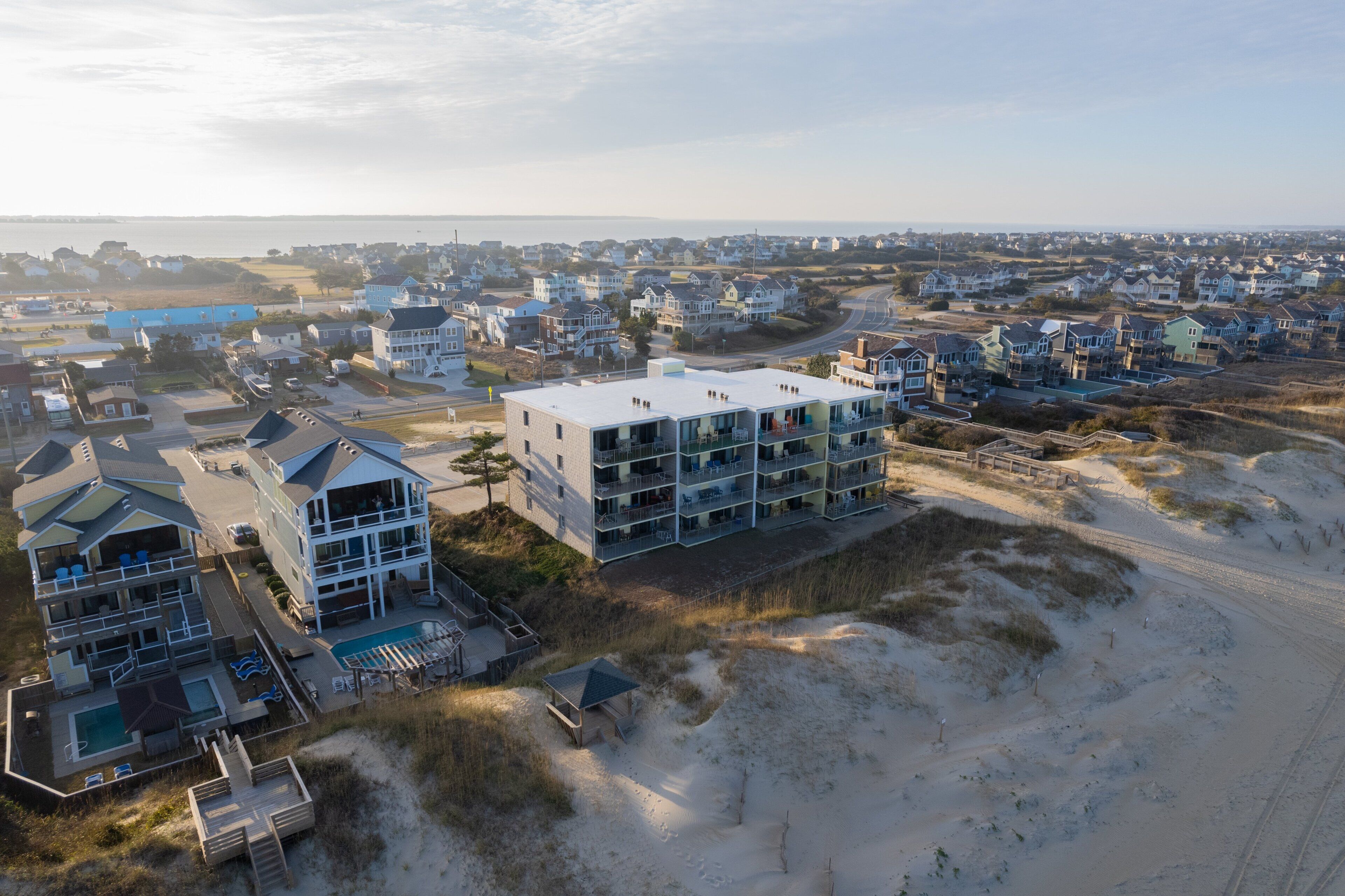 Una zona residenziale costiera con case moderne, un edificio di grandi dimensioni con numerosi balconi e una spiaggia sullo sfondo.