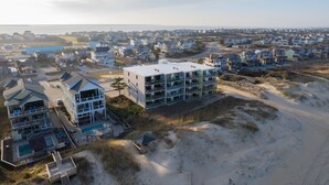 Zona residencial costera con casas modernas, un edificio grande con varios balcones y una playa al fondo.