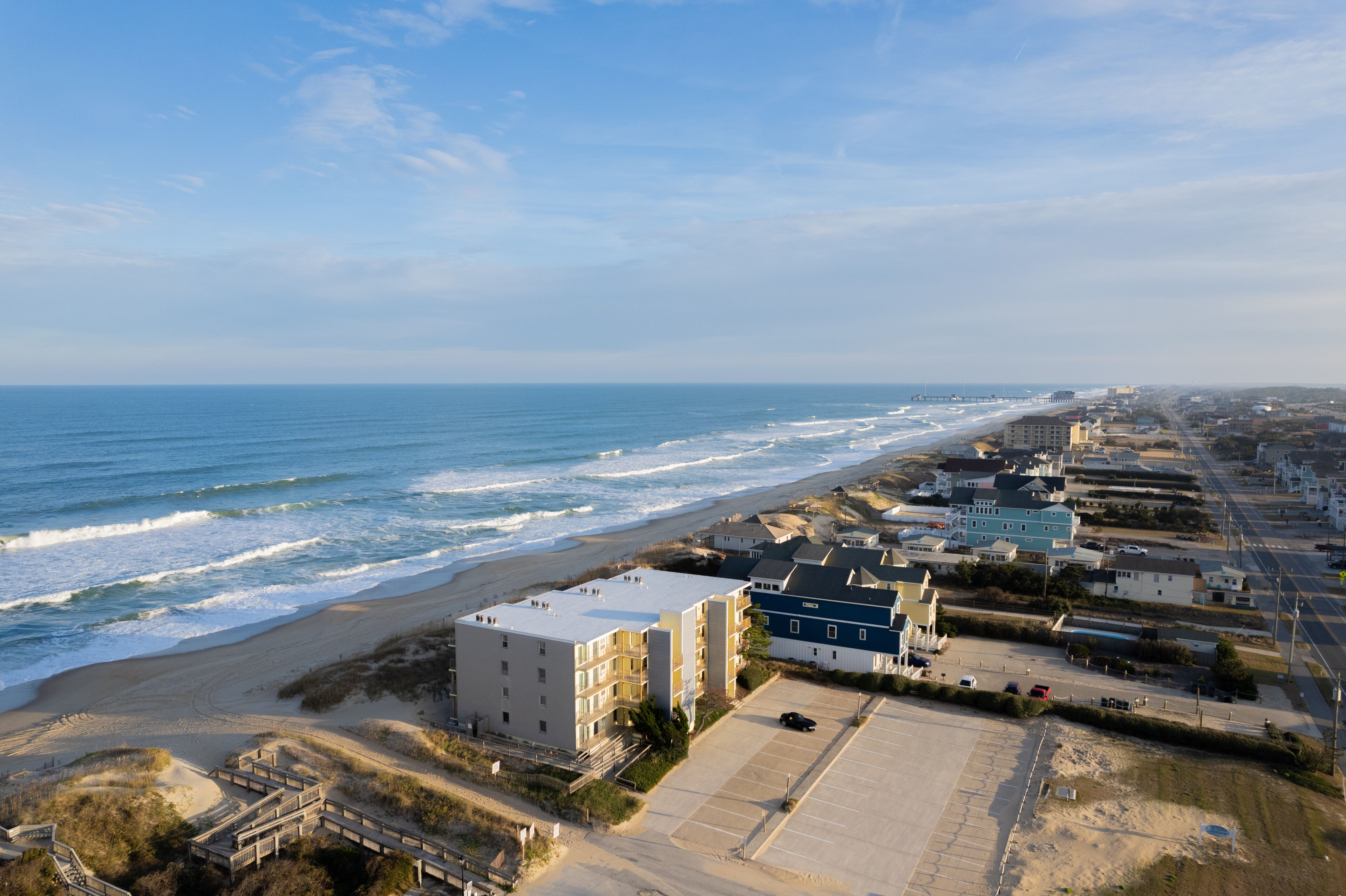 A coastal hotel with multiple buildings, a parking lot, and a beach view.