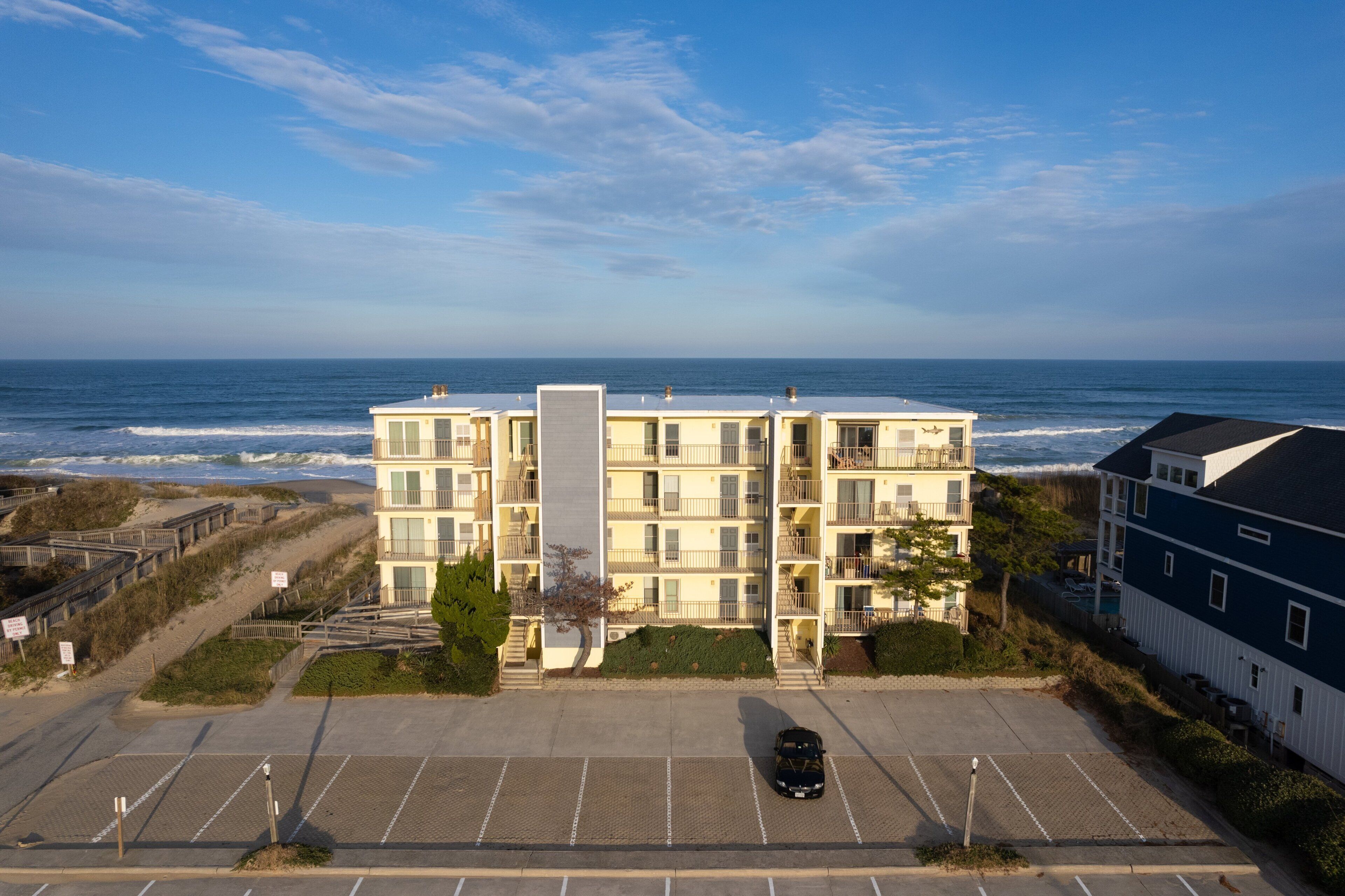A multi-story building with a parking lot in front, overlooking the ocean.