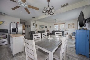 A dining area with a table and chairs, a ceiling fan, and a kitchen with appliances. - 7602- Drydock, Dog-Friendly Avon Cottage Near the Beach (Avon)