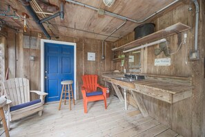 A rustic wooden room with a blue door, a wooden bench, a red chair, a bar area, and a sign indicating a fish cleaning station.